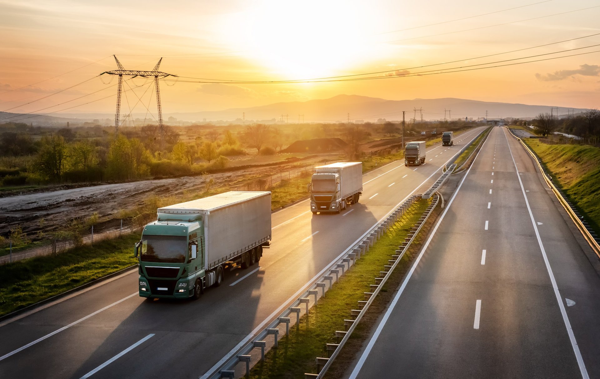 Convoy of professional trucks with containers on highway at sunset